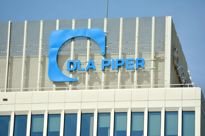 Blue logo of DLA Piper on a building, illuminated by the sun