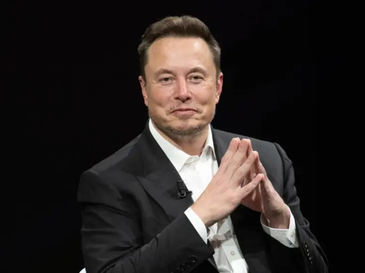 Elon Musk with his fingers together and slightly smiling