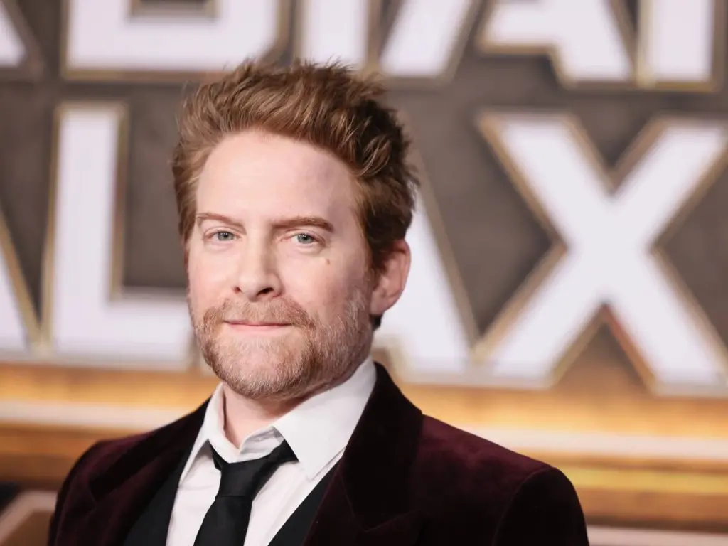 Actor Seth Green wearing a tie and standing in front of a step and repeat board