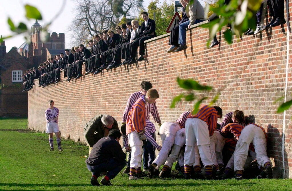 Eton's traditional wall game with boys in a scrum at the bottom on the wall while others sit on it and watch