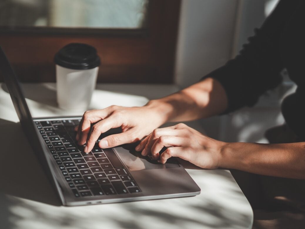 A man writing at a laptop with a takeaway coffee beside him