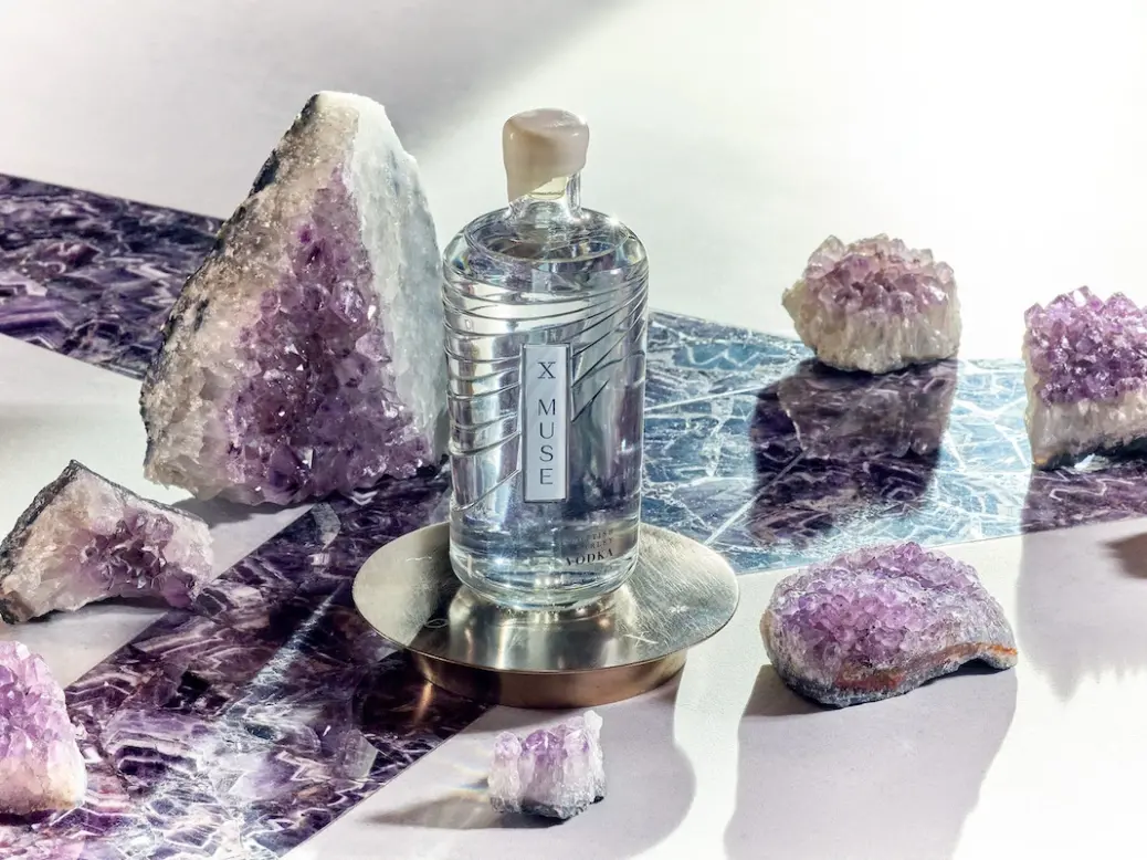 Bottle of X Muse vodka surrounded by amethyst crystals.