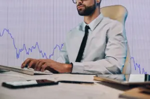 Man sitting at a computer with a stocks and shares chart behind