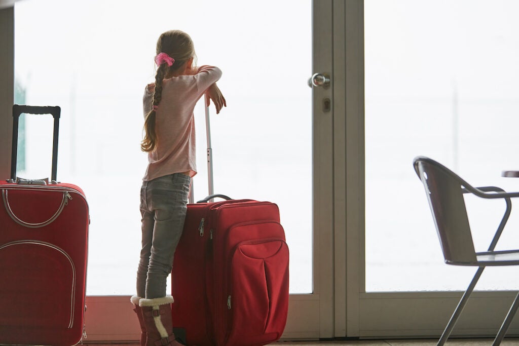 Little girl with suitcase is traveling alone, waiting for the flight in the airport terminal