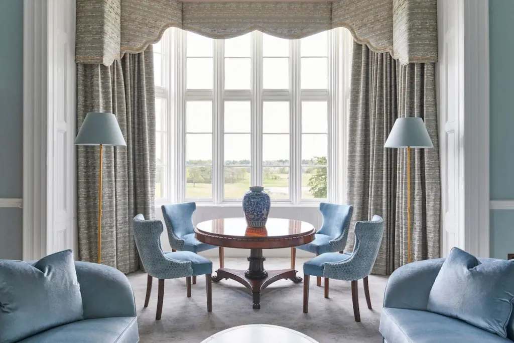 A table with four chairs in a bay window overlooking green space