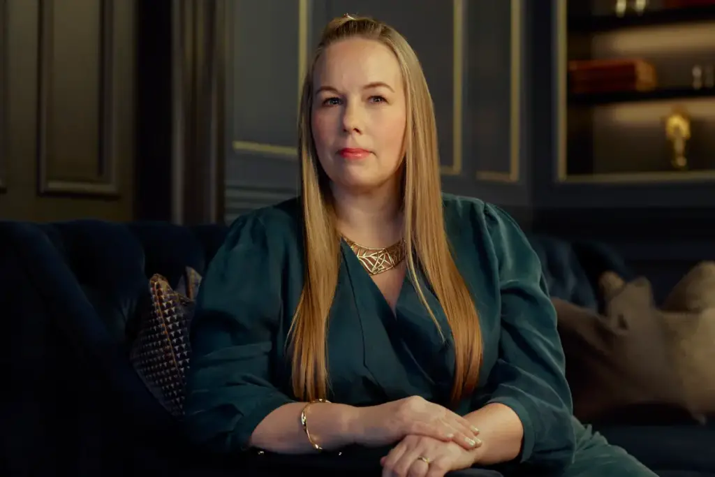 Ceri Griffiths wearing a green dress, leaning on a sofa arm