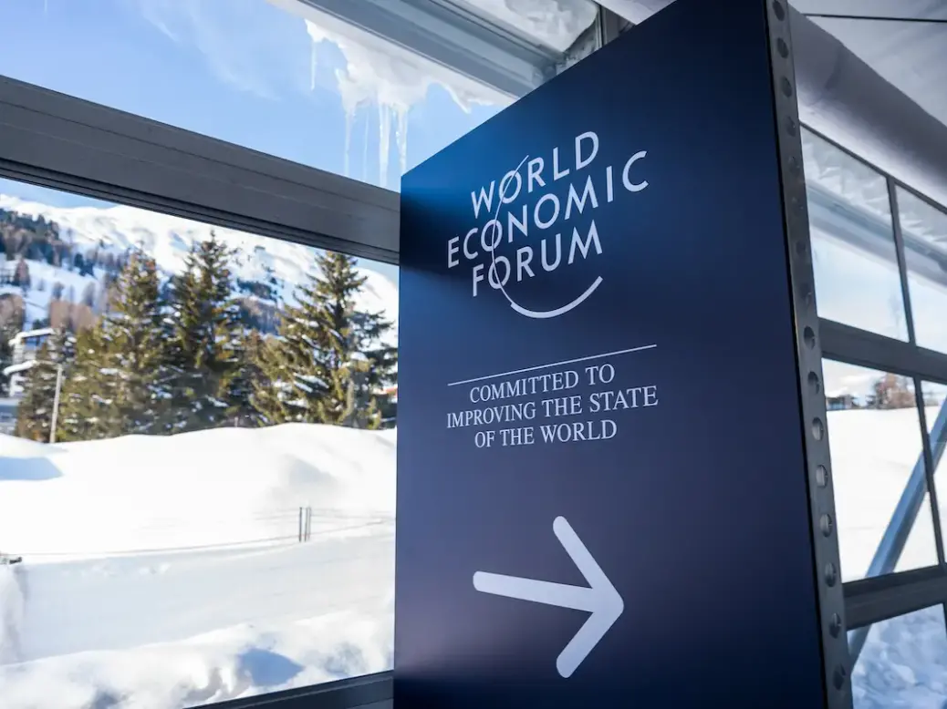 A sign saying World Economic Forum with an arrow pointing right outside is a snowy scene
