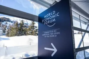 A sign saying World Economic Forum with an arrow pointing right outside is a snowy scene