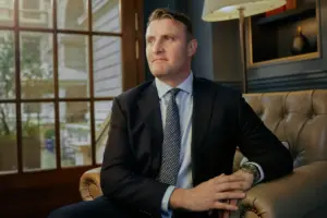 Ollie Barnett wearing a suit and spotted tie on an armchair