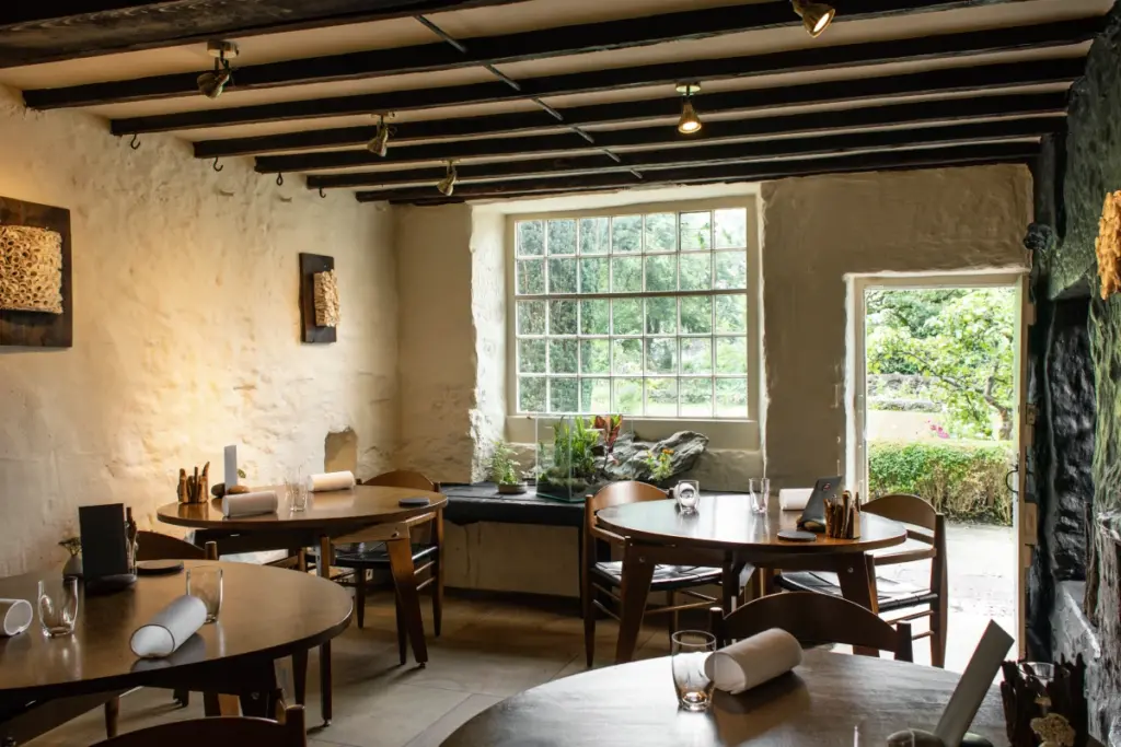 A small restaurant with menus and glasses on the table. The door is open to show the garden. It is a very old building with low ceilings