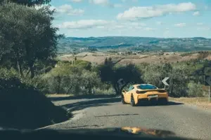 A yellow Ferrari drives through the Tuscan countryside