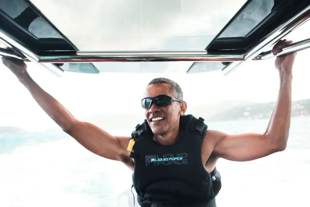 Barack Obama kitesurfing wearing a life jacket and sunglasses