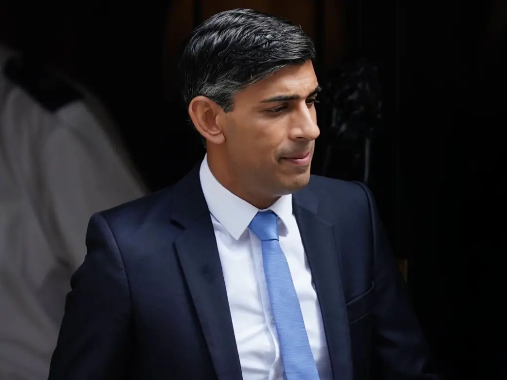 Rishi Sunak wearing a blue tie and suit looking towards the ground